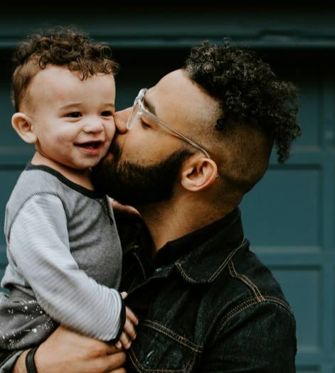 man carrying baby boy and kissing on cheek